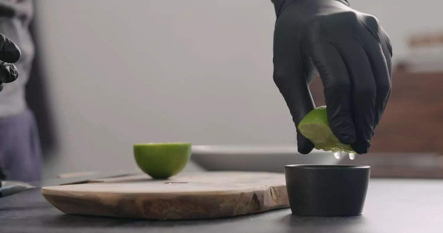 Black disposable gloves squeezing lime for food preparation