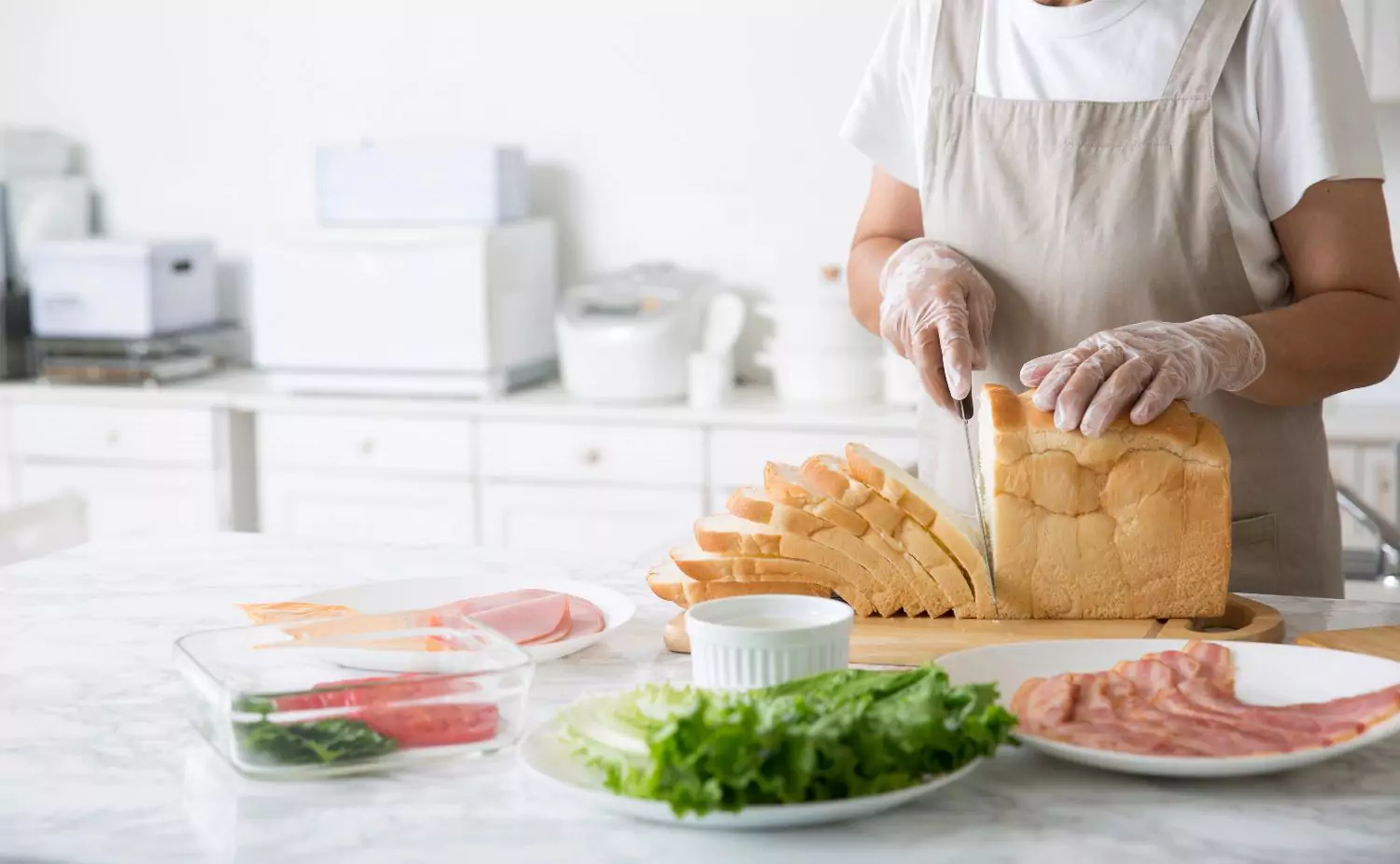Vinyl gloves being used to slice bread for sandwich preparation in a kitchen