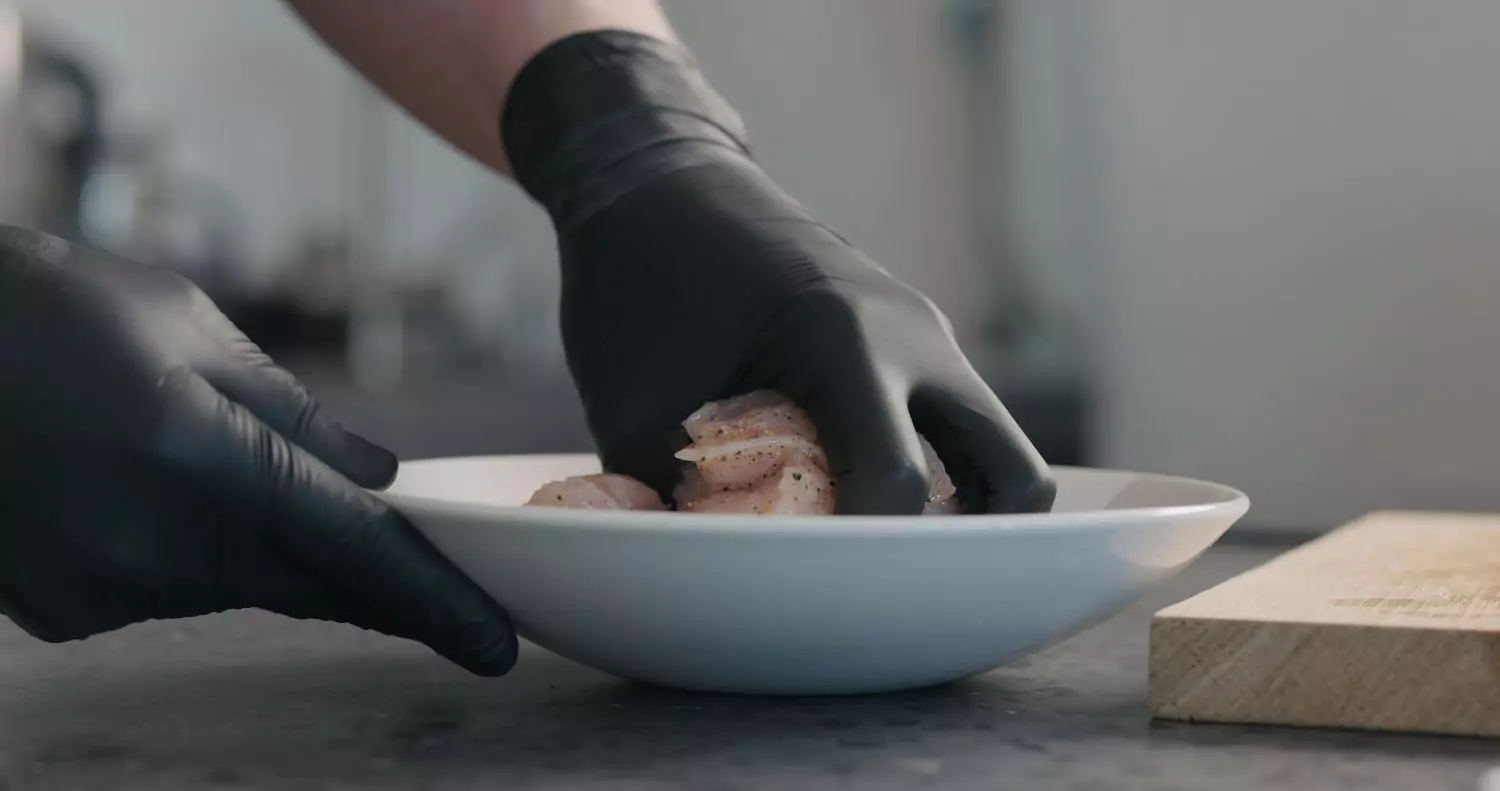 Black disposable gloves handling raw chicken in a kitchen food prep setting