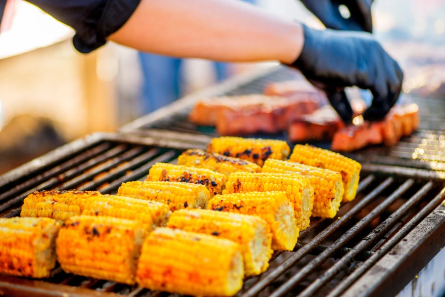 Grilled Corn on the Cob with Nitrile Gloves Handling Steaks at BBQ Party
